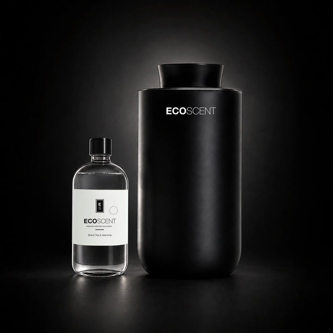 A matte black cylindrical EcoScent diffuser stands next to a clear glass bottle with a white label on a dark studio background.