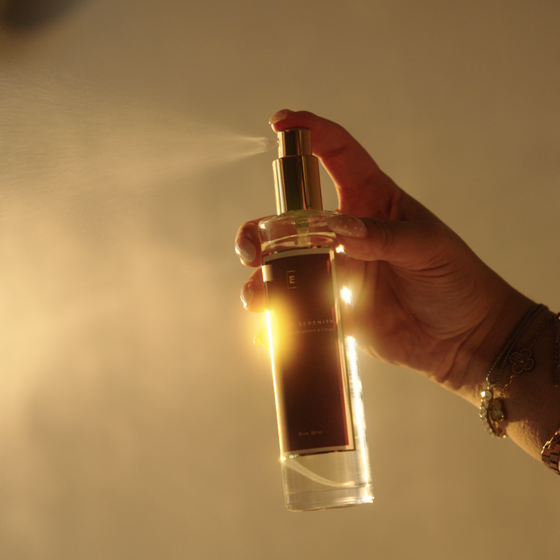 EcoScent Golden Serenity Comforting Room Spray, a 100ml clear glass bottle with a gold spray top and dark label, held in a hand as it mists.