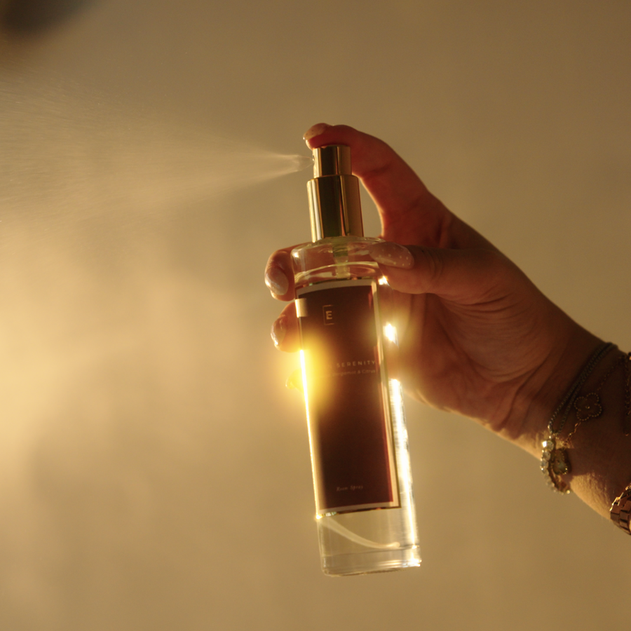 EcoScent Golden Serenity Comforting Room Spray, a 100ml clear glass bottle with a gold spray top and dark label, held in a hand as it mists.
