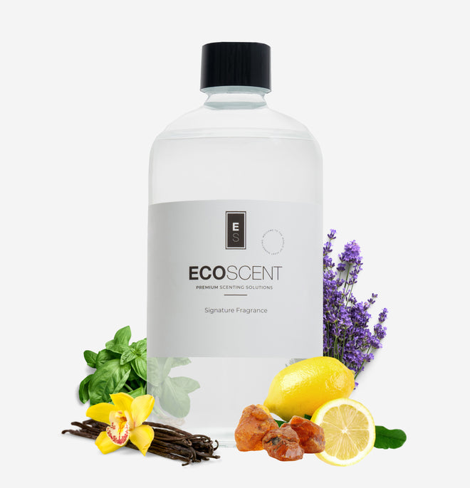 Ecoscent-shop Amber & Lavender Fragrance Oil in a clear glass bottle with a black cap, accompanied by lavender flowers, basil leaves, lemon, and vanilla. The label features the brand name and the description "Signature Fragrance."