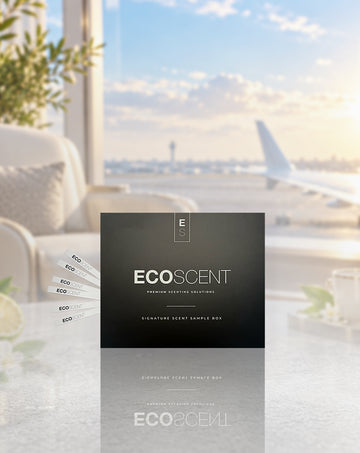 A black ECOSCENT premium scenting solution box is displayed on a reflective surface with a blurred airport scene in the background, including an airplane window view and lounge furniture.