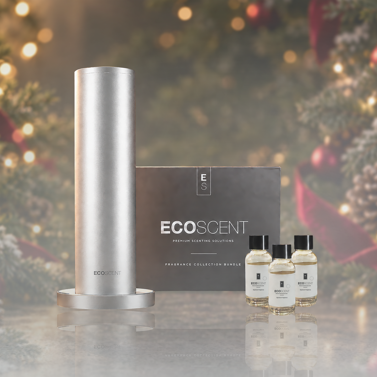 EcoScent The Scent of Christmas fragrance bundle with a silver cylindrical diffuser on a round base, a dark box, and three small glass bottles, set against a festive blurred background.