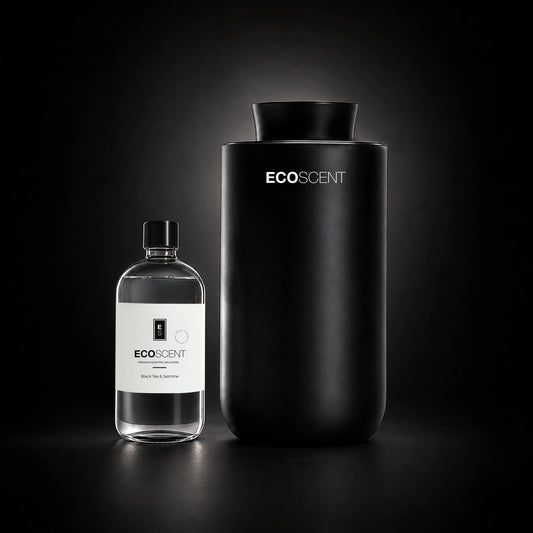 A matte black cylindrical EcoScent diffuser stands next to a clear glass bottle with a white label on a dark studio background.