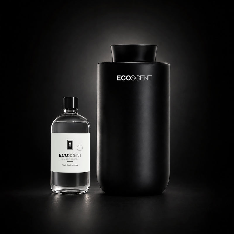 A matte black cylindrical EcoScent diffuser stands next to a clear glass bottle with a white label on a dark studio background.
