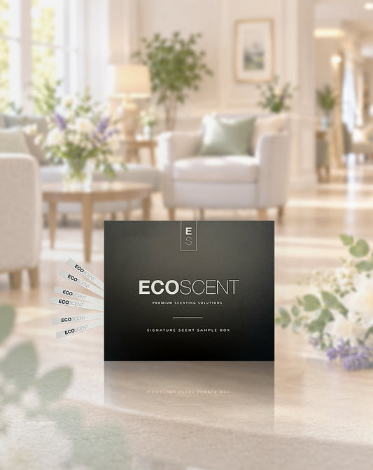 A black ECOSCENT premium setting sample box takes centre stage in the foreground, while several small scent sample cards fan out to the left. Behind it, a softly blurred, bright and elegant care home living room creates a warm backdrop.