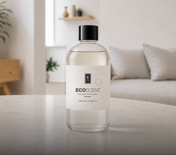 A clear glass bottle of ECOSCENT Signature Fragrance with a black cap and white label, set on a light-colored table in a softly blurred modern living room background.