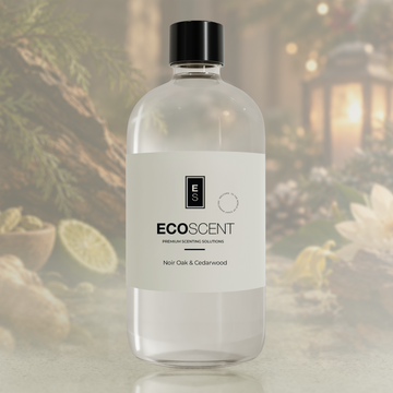 A clear glass bottle of ECOSCENT Premium Scenting Solutions in the Noir Oak & Cedarwood scent, featuring a white label and a black cap, set against a softly blurred background of greenery and warm lantern light.