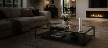 Modern living room with beige sofa, glass coffee table, scent machine and lit fireplace, featuring books, plants, and decor for a cosy atmosphere.
