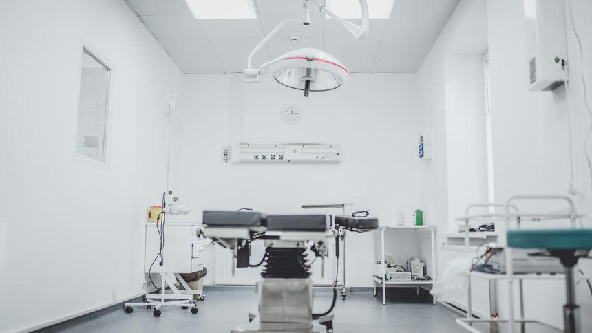 Sterile medical room featuring an examination table, a surgical light overhead, and medical equipment including a trolley and various instruments.