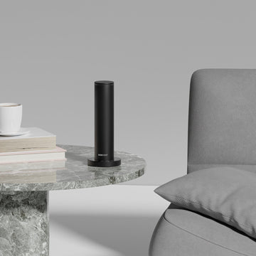 Black cylindrical scent machine on a marble side table next to a gray sofa.