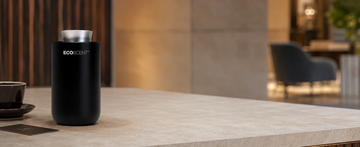 A matte black cylindrical ECO SCENT diffuser with a silver top, placed on a light stone countertop in a modern, softly blurred indoor setting.
