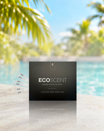 A black EcoScent premium testing solution sample box stands on a light stone surface with a blurred swimming pool and palm trees in the background. Several small test strips are fanned out to the left.